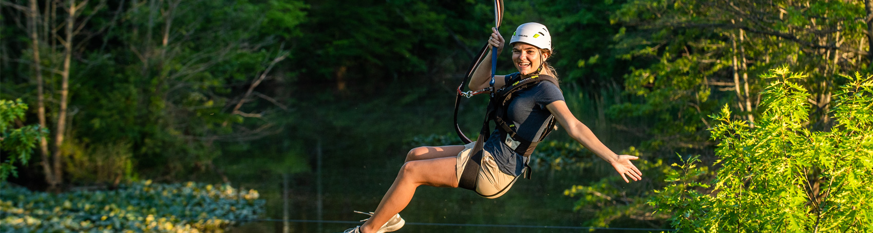 Smiling girl on a zipline with her left arm sticking out